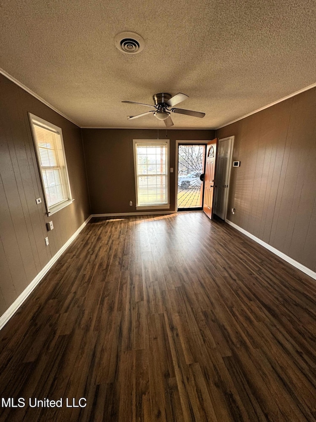 spare room with visible vents, crown molding, baseboards, a ceiling fan, and dark wood-style flooring