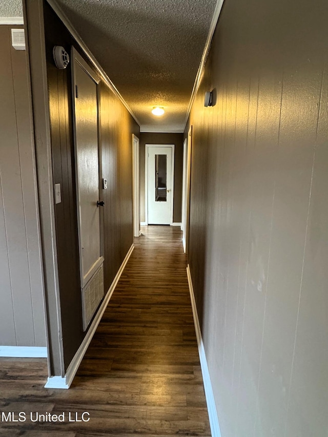 hallway featuring baseboards, a textured ceiling, ornamental molding, and dark wood-style flooring