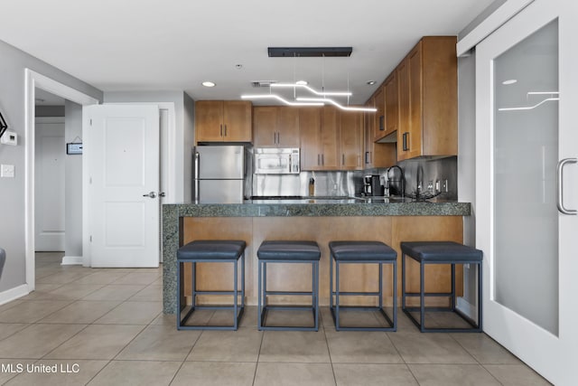 2060 Beach Blvd Unit 102, Biloxi, MS 39531 - kitchen with stainless steel appliances, dark countertops, a peninsula, brown cabinets, and light tile patterned flooring