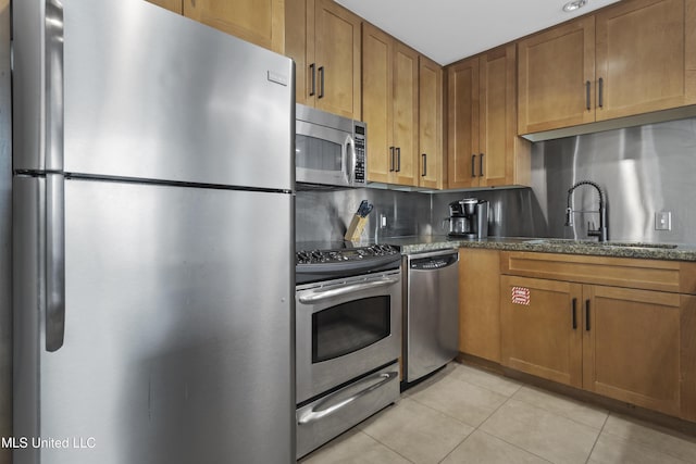 2060 Beach Blvd Unit 102, Biloxi, MS 39531 - kitchen with stainless steel appliances, light tile patterned floors, dark stone countertops, brown cabinets, and tasteful backsplash