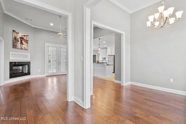 unfurnished living room with a multi sided fireplace, wood-type flooring, ceiling fan with notable chandelier, and crown molding