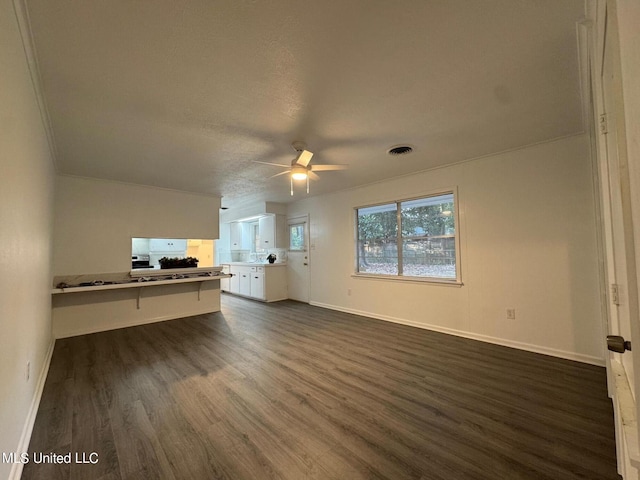 unfurnished living room featuring ornamental molding, dark wood-type flooring, a textured ceiling, and ceiling fan