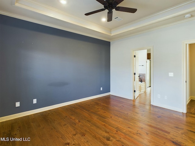 empty room with a raised ceiling, ceiling fan, dark wood-type flooring, and ornamental molding