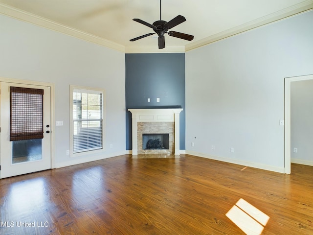 unfurnished living room featuring ceiling fan, a tiled fireplace, ornamental molding, and hardwood / wood-style flooring