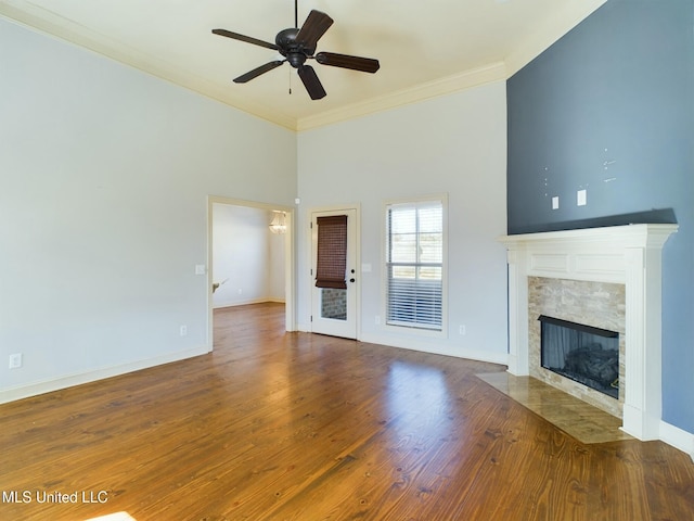 unfurnished living room featuring ceiling fan, a fireplace, hardwood / wood-style floors, a towering ceiling, and ornamental molding