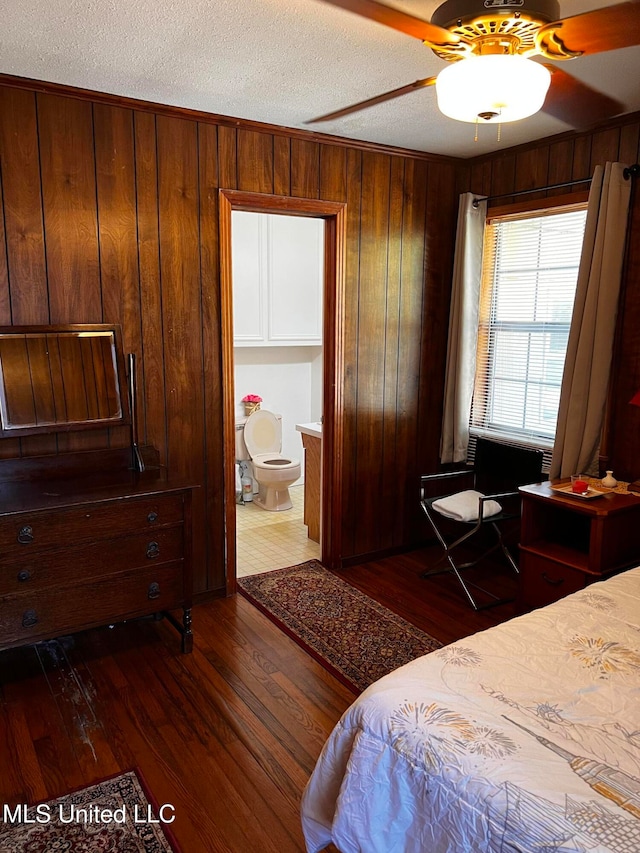 bedroom featuring connected bathroom, ceiling fan, dark hardwood / wood-style flooring, a textured ceiling, and wooden walls