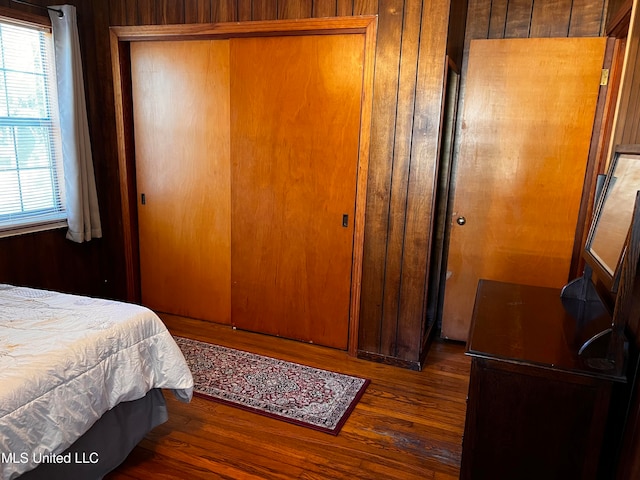 bedroom featuring dark hardwood / wood-style floors, wooden walls, and a closet