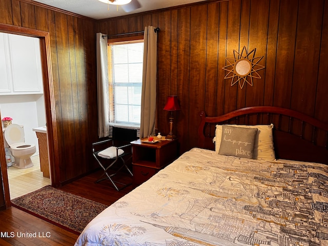 bedroom with ensuite bathroom, wood-type flooring, and wooden walls