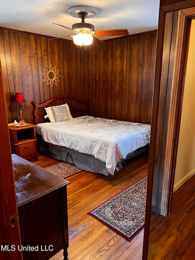 bedroom with wood-type flooring, ceiling fan, and wooden walls