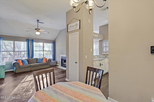 dining space with visible vents, a fireplace with flush hearth, dark wood-style floors, and vaulted ceiling