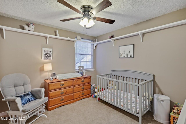 carpeted bedroom featuring a nursery area, a textured ceiling, and a ceiling fan
