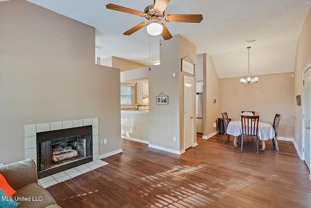 living area with ceiling fan with notable chandelier, a tile fireplace, wood finished floors, and lofted ceiling
