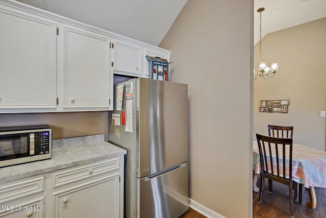 kitchen featuring white cabinets, appliances with stainless steel finishes, lofted ceiling, and a chandelier