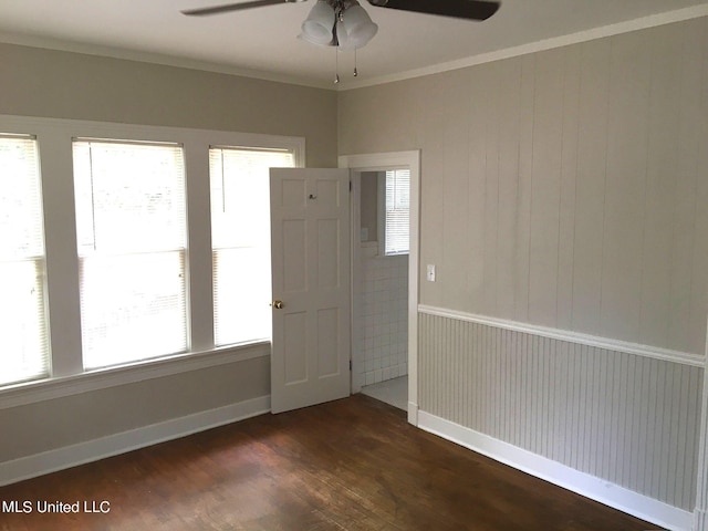 empty room with crown molding, wood walls, dark hardwood / wood-style floors, and ceiling fan