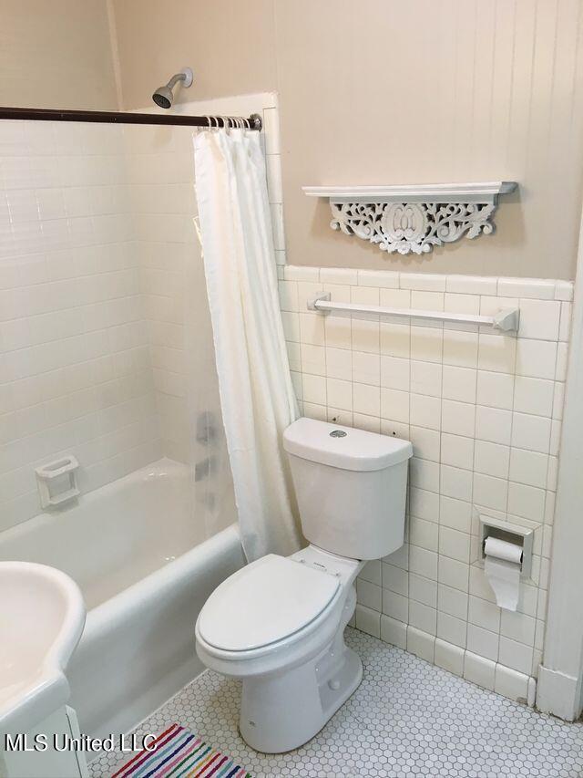 bathroom with toilet, shower / bath combo with shower curtain, tile walls, and tile patterned flooring