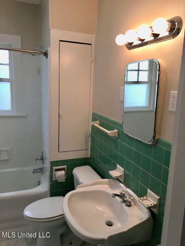 full bathroom featuring toilet, sink, tile walls, and tub / shower combination