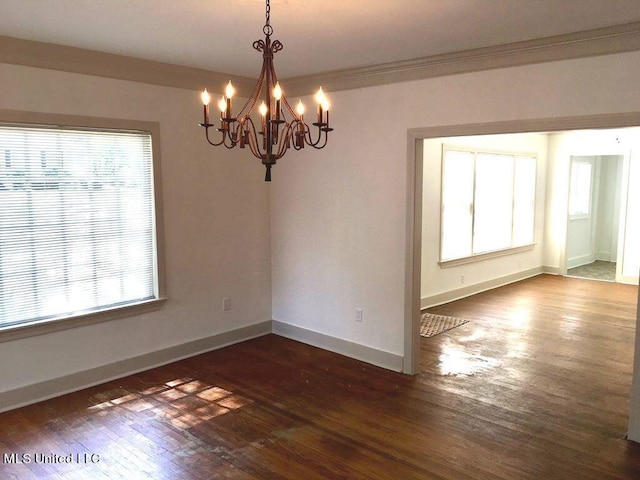 spare room with dark wood-type flooring, a wealth of natural light, and a chandelier