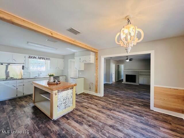 kitchen with white cabinetry, dark wood-type flooring, pendant lighting, and ceiling fan with notable chandelier