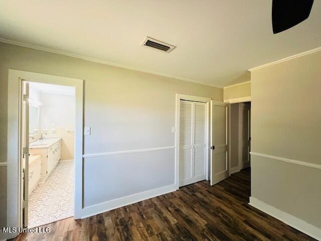 unfurnished bedroom featuring dark wood-type flooring, connected bathroom, a closet, and ornamental molding