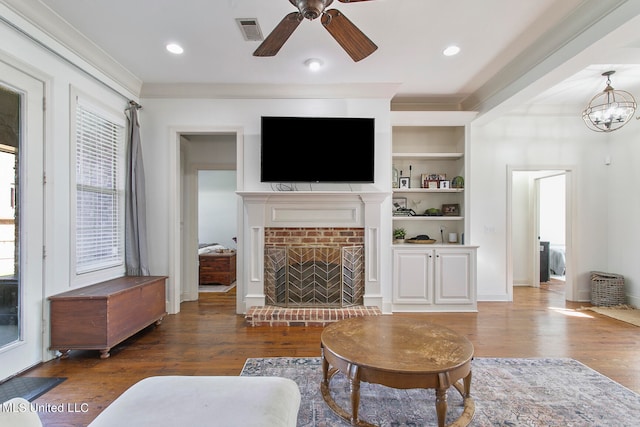 living room with dark hardwood / wood-style floors, built in shelves, ceiling fan with notable chandelier, and a brick fireplace