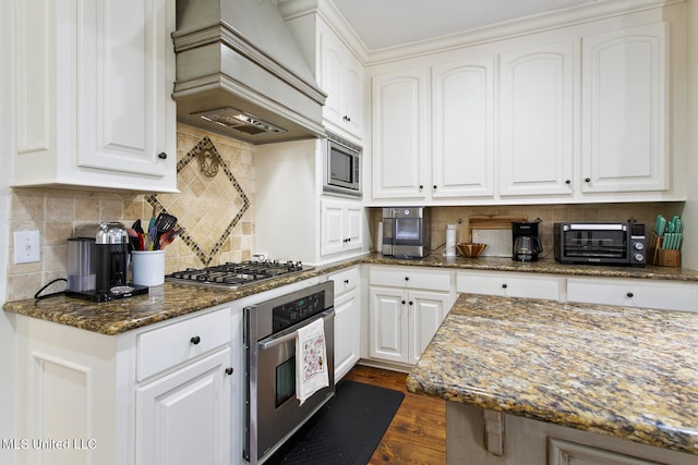 kitchen with dark hardwood / wood-style flooring, stainless steel appliances, custom exhaust hood, white cabinets, and dark stone countertops