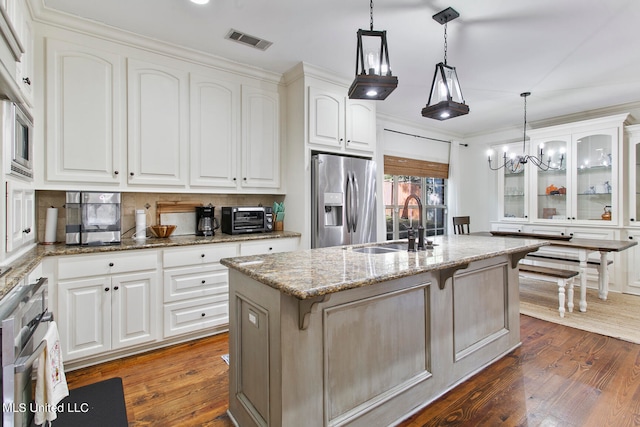 kitchen featuring light stone countertops, appliances with stainless steel finishes, a center island with sink, and white cabinets