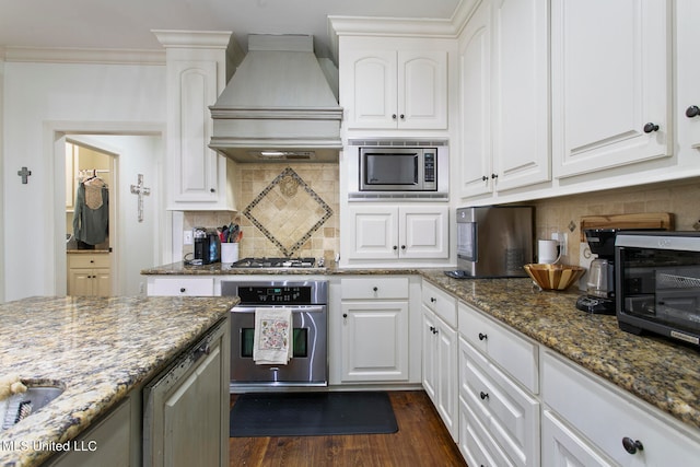 kitchen with white cabinets, dark stone counters, custom range hood, dark wood-type flooring, and stainless steel appliances