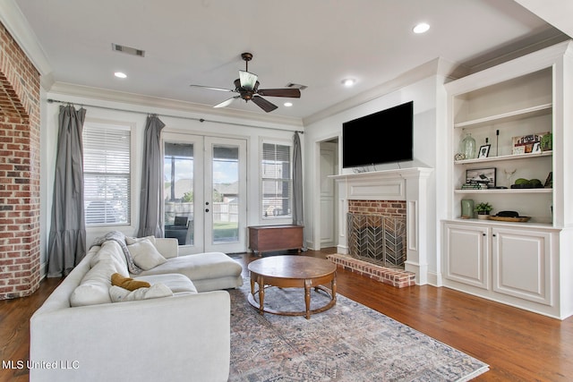 living room featuring crown molding, built in features, dark hardwood / wood-style flooring, a fireplace, and ceiling fan