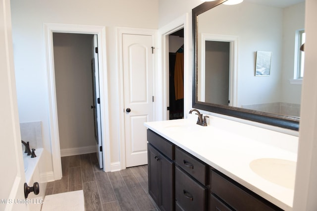 full bathroom with baseboards, double vanity, a sink, and wood tiled floor