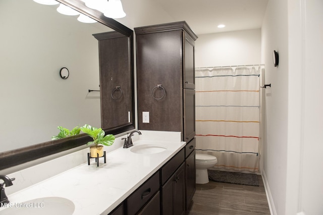 bathroom featuring double vanity, wood finished floors, a sink, and toilet