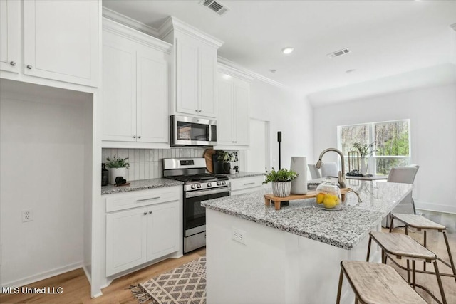 213 Dolly Ln, Magee, MS 39111 - kitchen with appliances with stainless steel finishes, light wood-type flooring, a center island with sink, white cabinetry, and baseboards