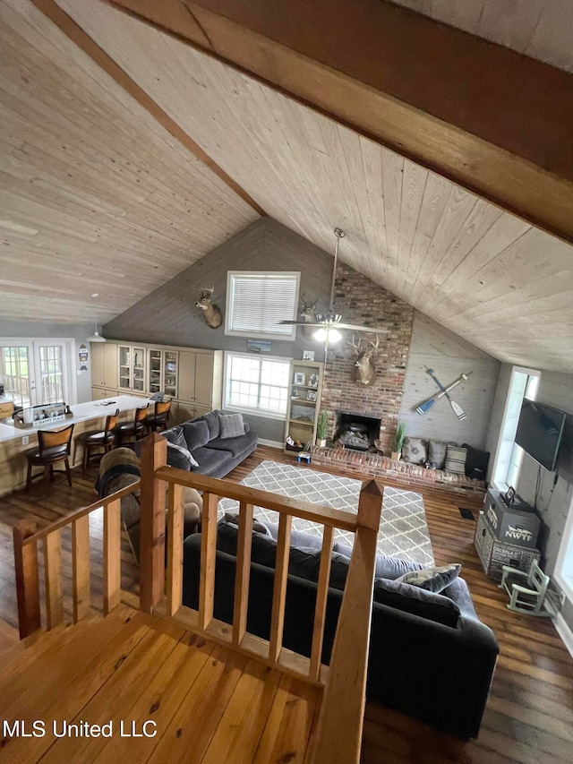 living room with a wealth of natural light, beam ceiling, wood-type flooring, and a large fireplace