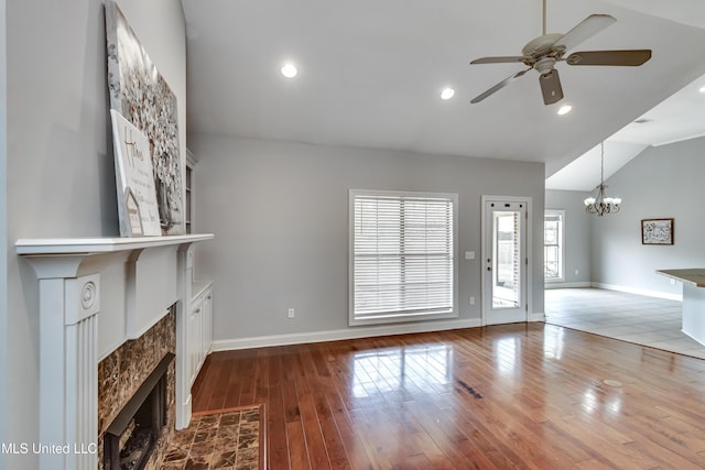 unfurnished living room featuring hardwood / wood-style flooring, a tiled fireplace, vaulted ceiling, and ceiling fan with notable chandelier