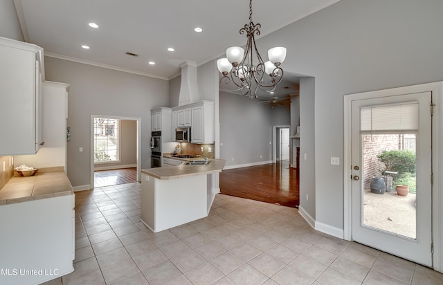 kitchen featuring a towering ceiling, pendant lighting, white cabinets, light tile patterned floors, and stainless steel appliances