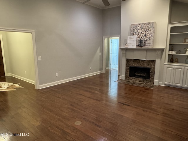 unfurnished living room featuring dark wood-type flooring, ceiling fan, a premium fireplace, and a high ceiling