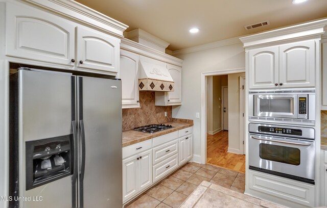 kitchen with light tile patterned flooring, white cabinetry, backsplash, and appliances with stainless steel finishes