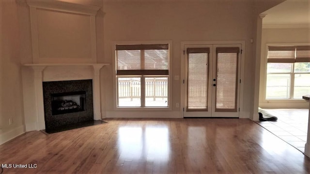 unfurnished living room featuring french doors, light wood-type flooring, plenty of natural light, and crown molding