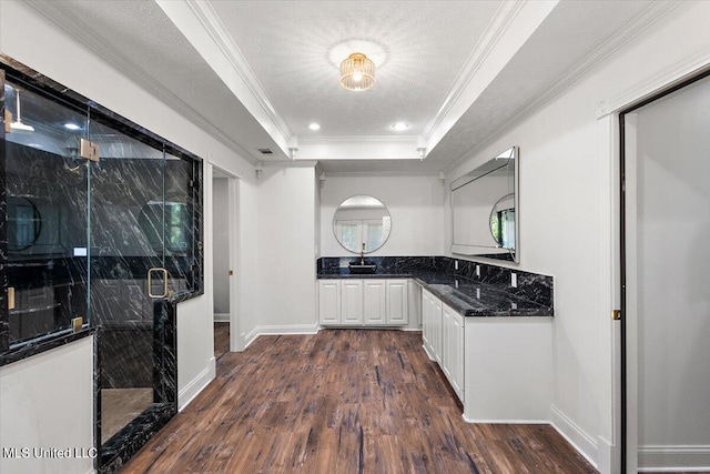 kitchen with a textured ceiling, a tray ceiling, white cabinets, dark wood-type flooring, and crown molding