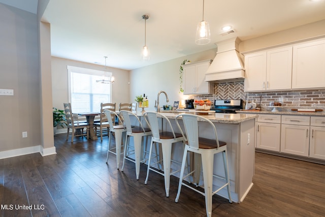 kitchen with stainless steel range oven, white cabinetry, decorative light fixtures, premium range hood, and a kitchen island with sink