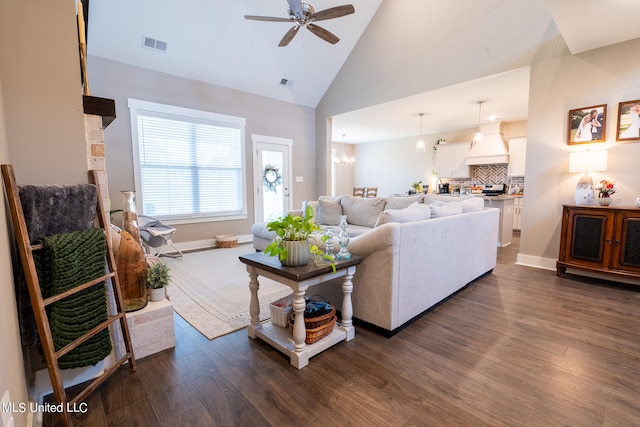 living room featuring dark wood-type flooring, ceiling fan with notable chandelier, and high vaulted ceiling