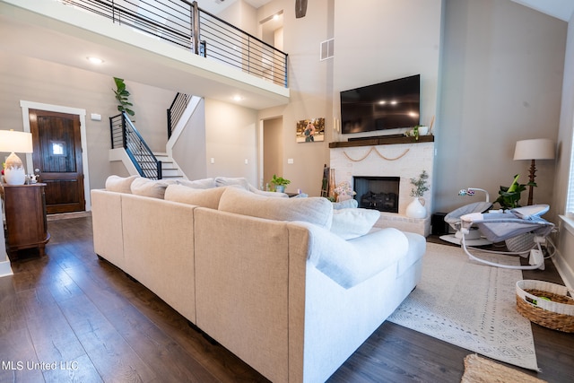 living room with a towering ceiling, dark wood-type flooring, and a brick fireplace