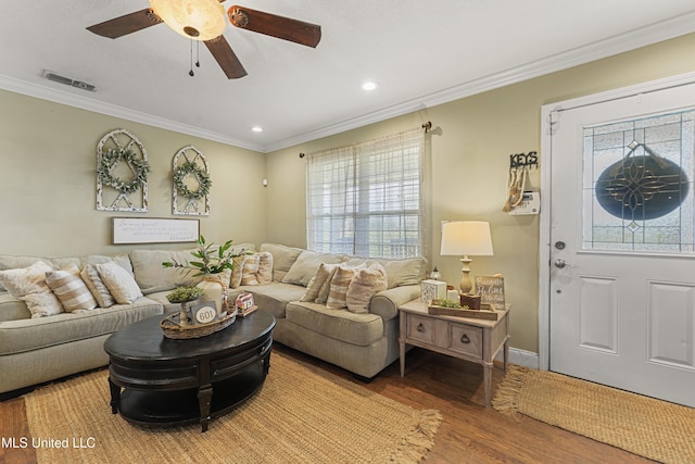 living area with visible vents, wood finished floors, ceiling fan, and ornamental molding