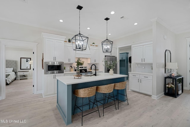 kitchen featuring light hardwood / wood-style flooring, appliances with stainless steel finishes, white cabinetry, a kitchen island with sink, and a kitchen bar