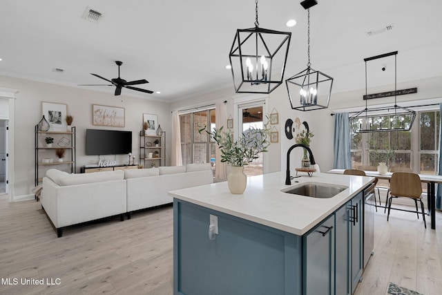 kitchen with pendant lighting, ornamental molding, sink, and a center island with sink