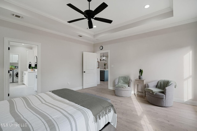 bedroom featuring ornamental molding, washing machine and clothes dryer, light hardwood / wood-style floors, and a tray ceiling