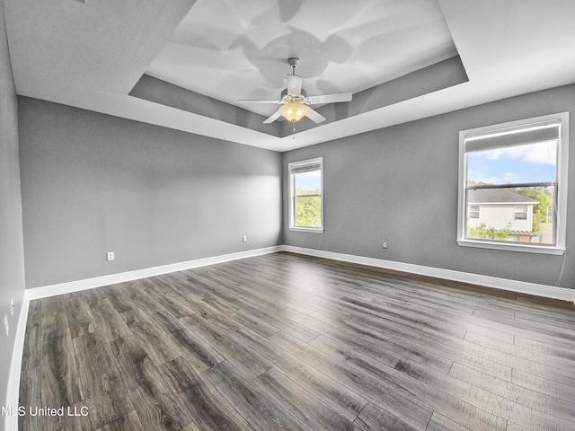 empty room with a raised ceiling, baseboards, a ceiling fan, and dark wood-style floors