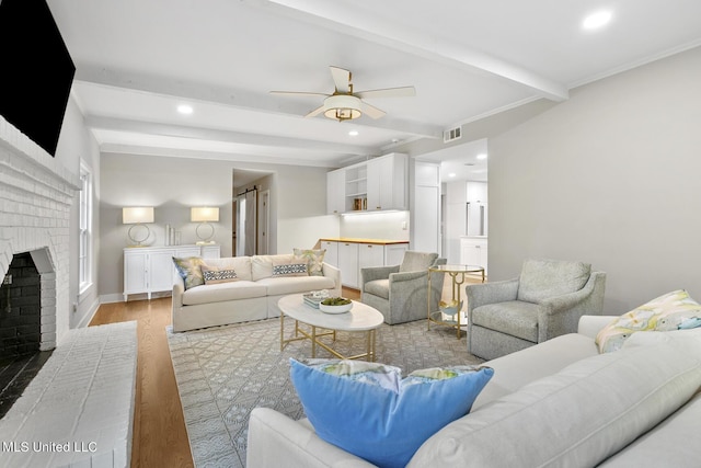 living area featuring recessed lighting, visible vents, light wood-style floors, a brick fireplace, and beamed ceiling