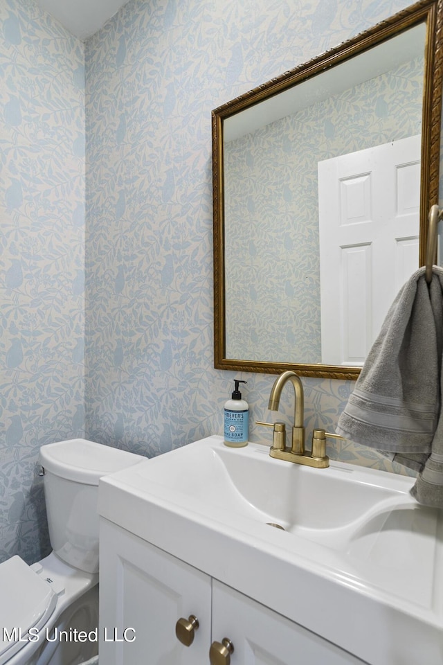 bathroom with vanity, toilet, and wallpapered walls