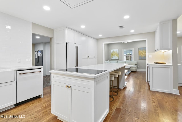 kitchen featuring visible vents, white cabinets, dishwasher, light wood-style flooring, and backsplash