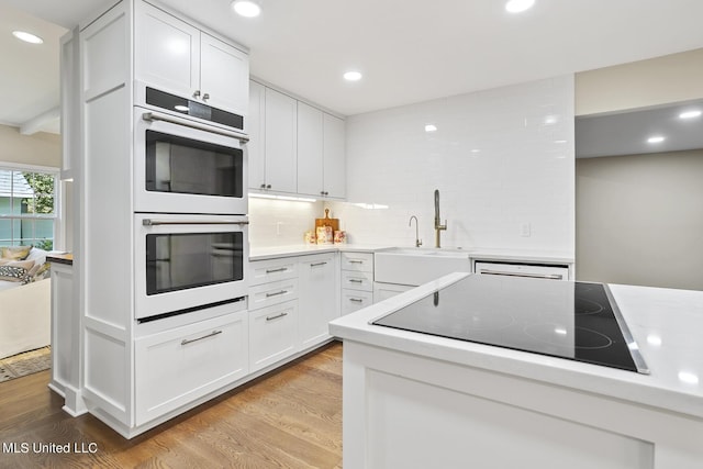 kitchen with light wood finished floors, black electric cooktop, light countertops, double oven, and a sink